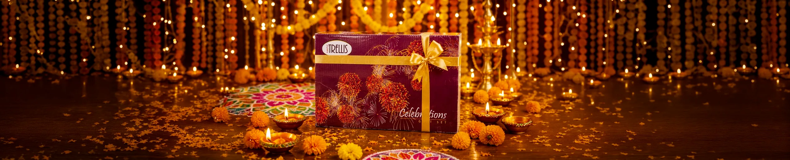 A gift box tied with a ribbon, on a table with diyas, marigolds and festival lights.