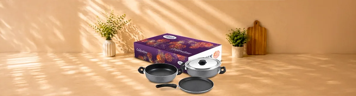 Grey non-stick kadai, tawa and lidded pan before a purple gift box