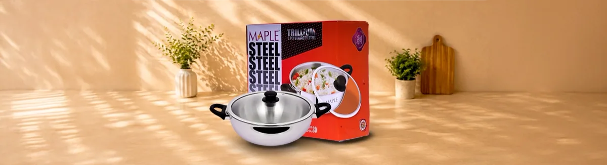 Steel kadai with black side handles and a glass lid, red box behind