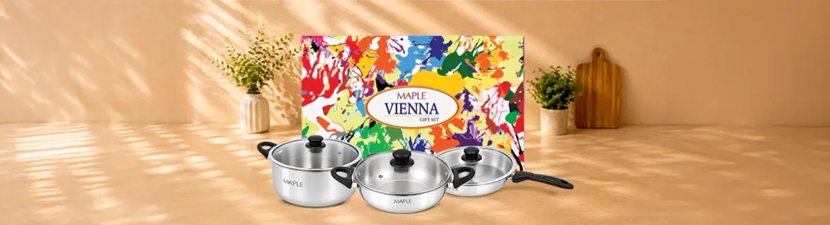 Two steel pots with glass lids and a fry pan, colourful gift box behind