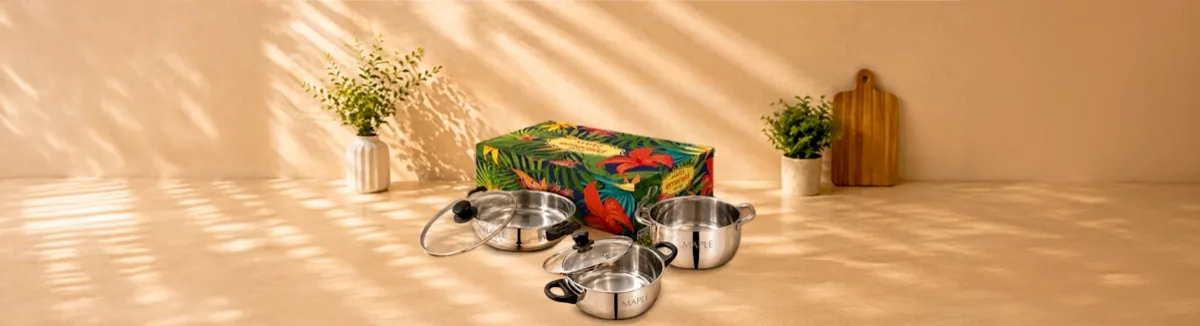 Three steel pots with glass lids and black knobs, beside a printed box