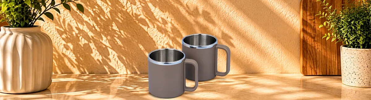 Two grey double-walled steel mugs with square handles, on a kitchen counter